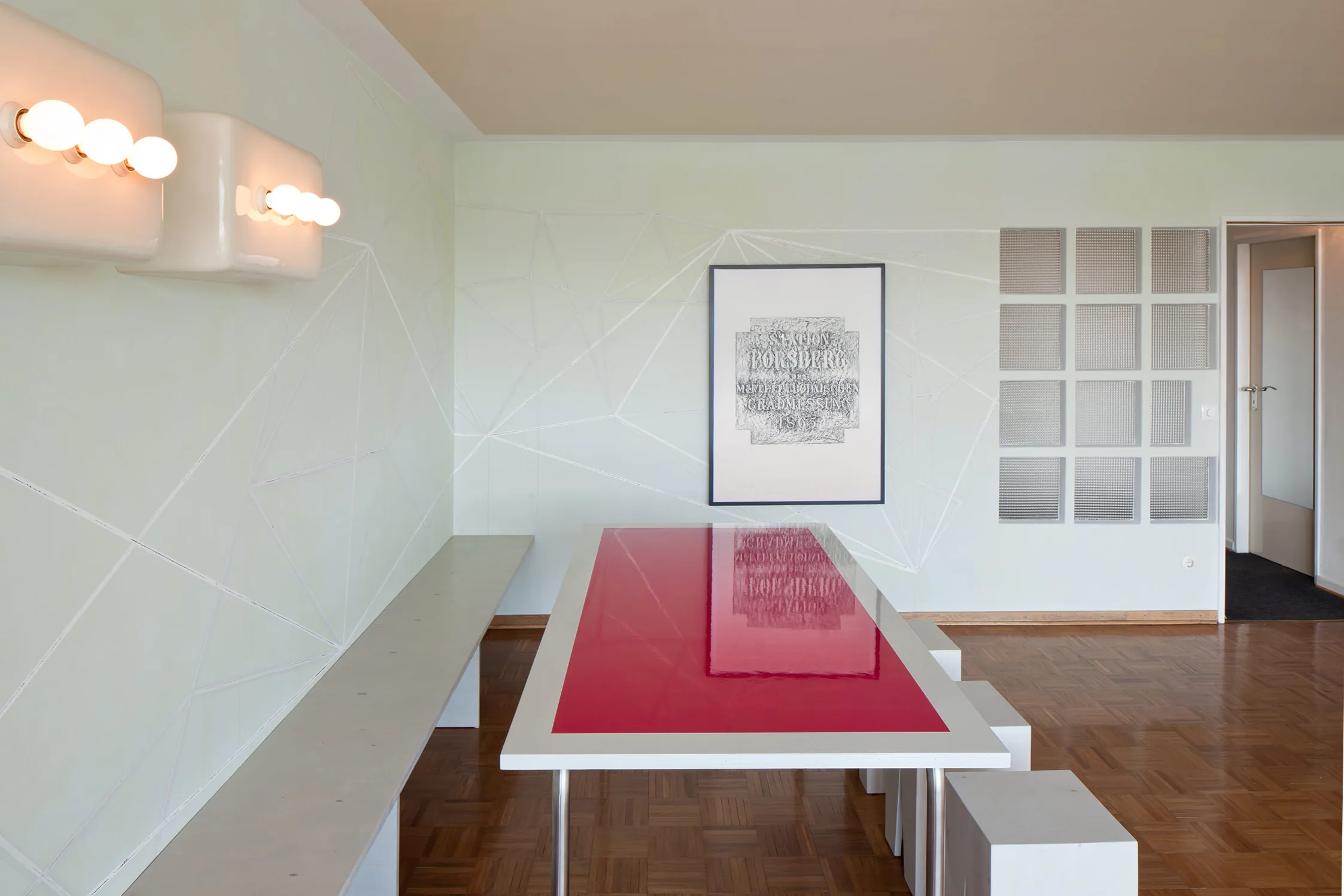 Verlasse mich nie — Blick in den Wohnraum mit Bank, himbeerrotem Tisch und der gerahmten Algrafie an der Wand